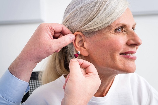 Ältere Frau bekommt ein Hörgerät eingesetzt, Hörakustiker berät zu Hörhilfen.